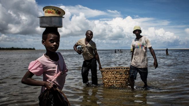 girl-standing-in-water-to-buy-fish-from-fishermen-with-basket