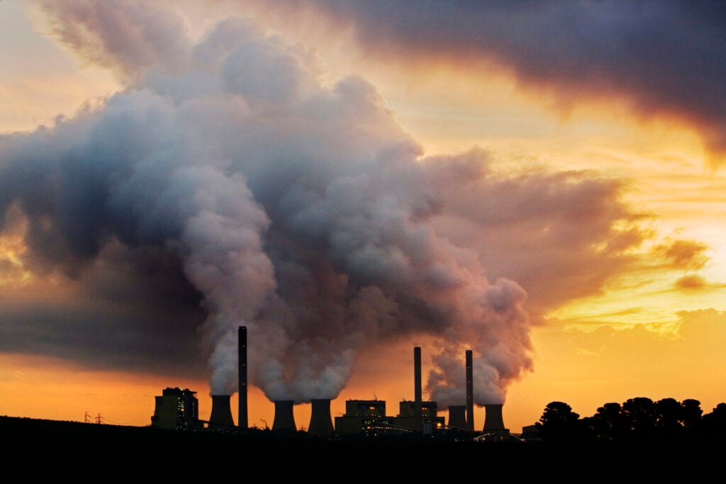 Power plant emitting steam and smoke at sunset.